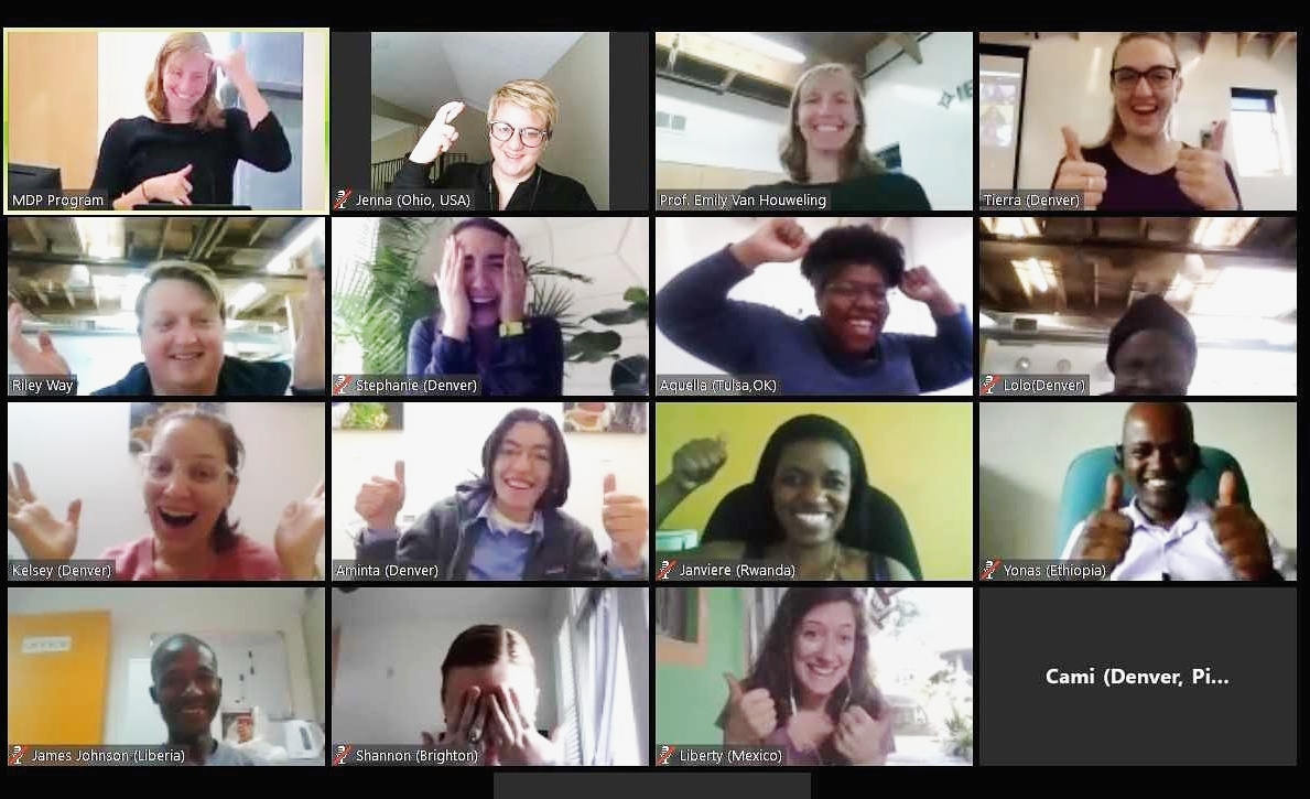 A screenshot of 16 participants during an online praxis course, making hand gestures and smiling for a group check-in